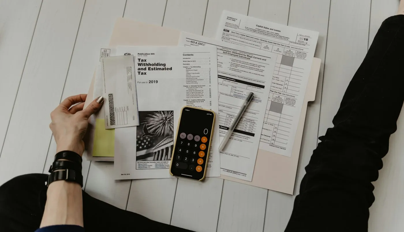 Hands sorting tax forms and receipts beside a calculator on a desk