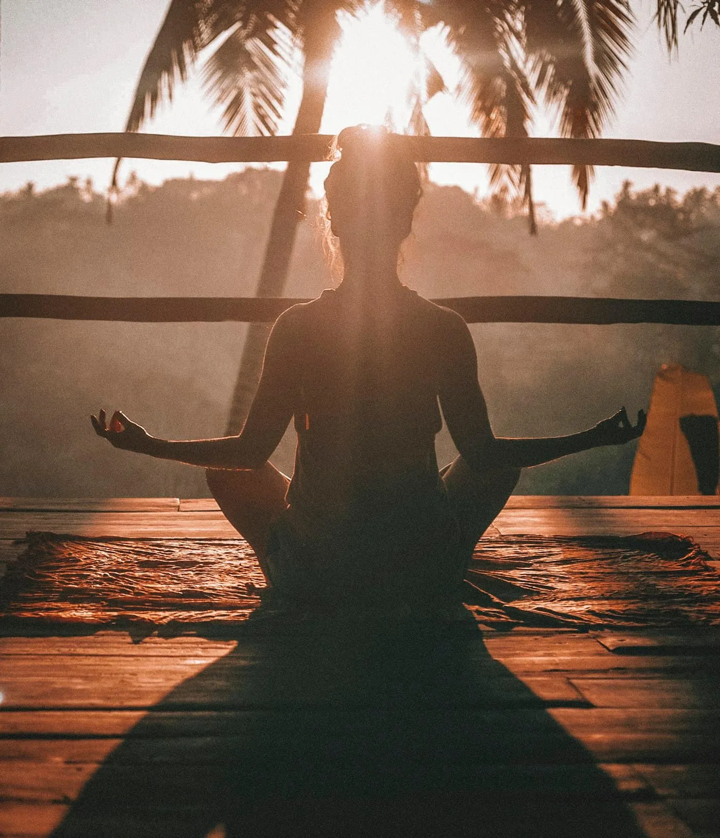 Silhouette of a person meditating cross-legged by a window in warm light