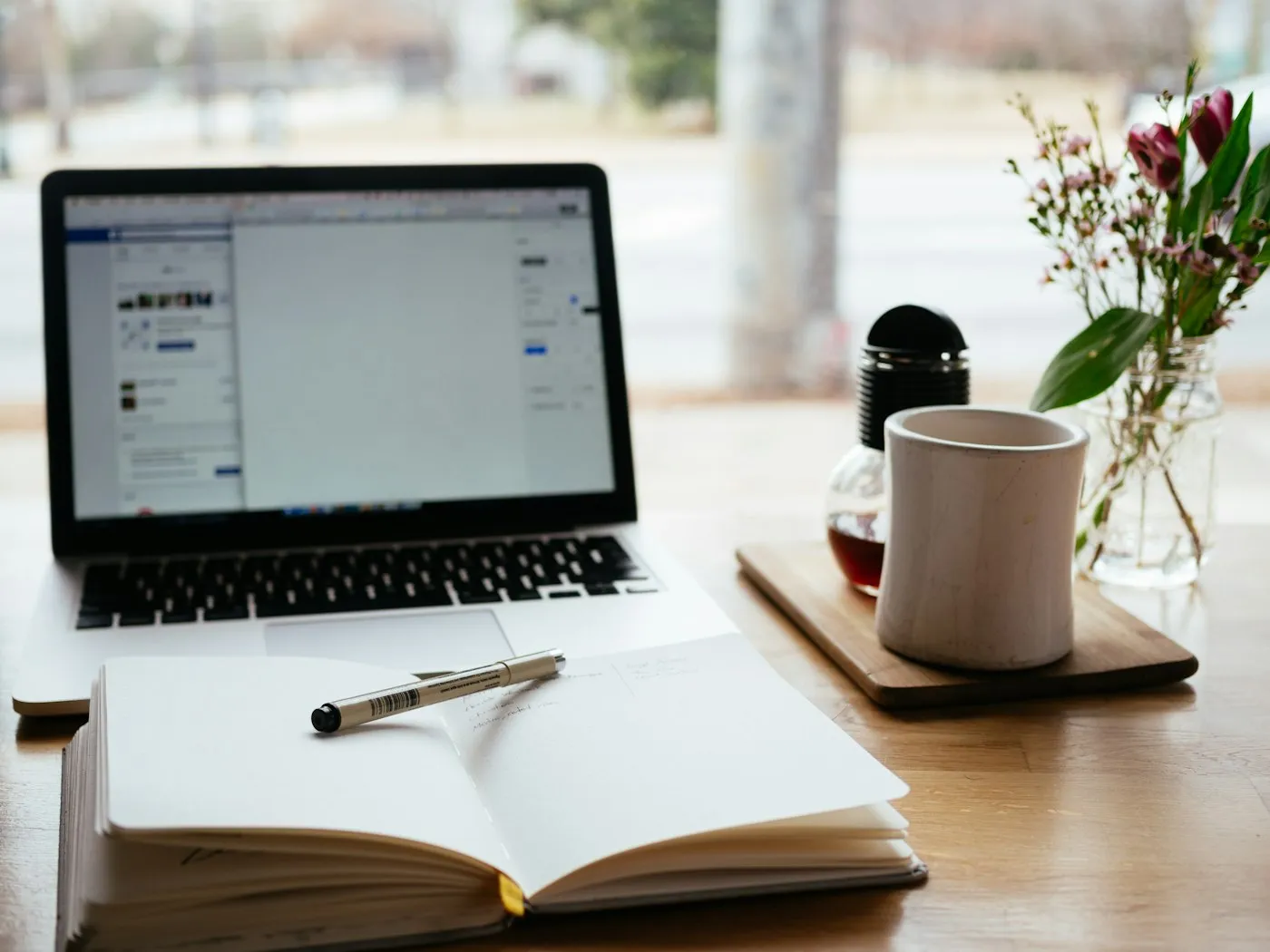 Open notebook and laptop on a desk beside a cup of coffee, ready for reading