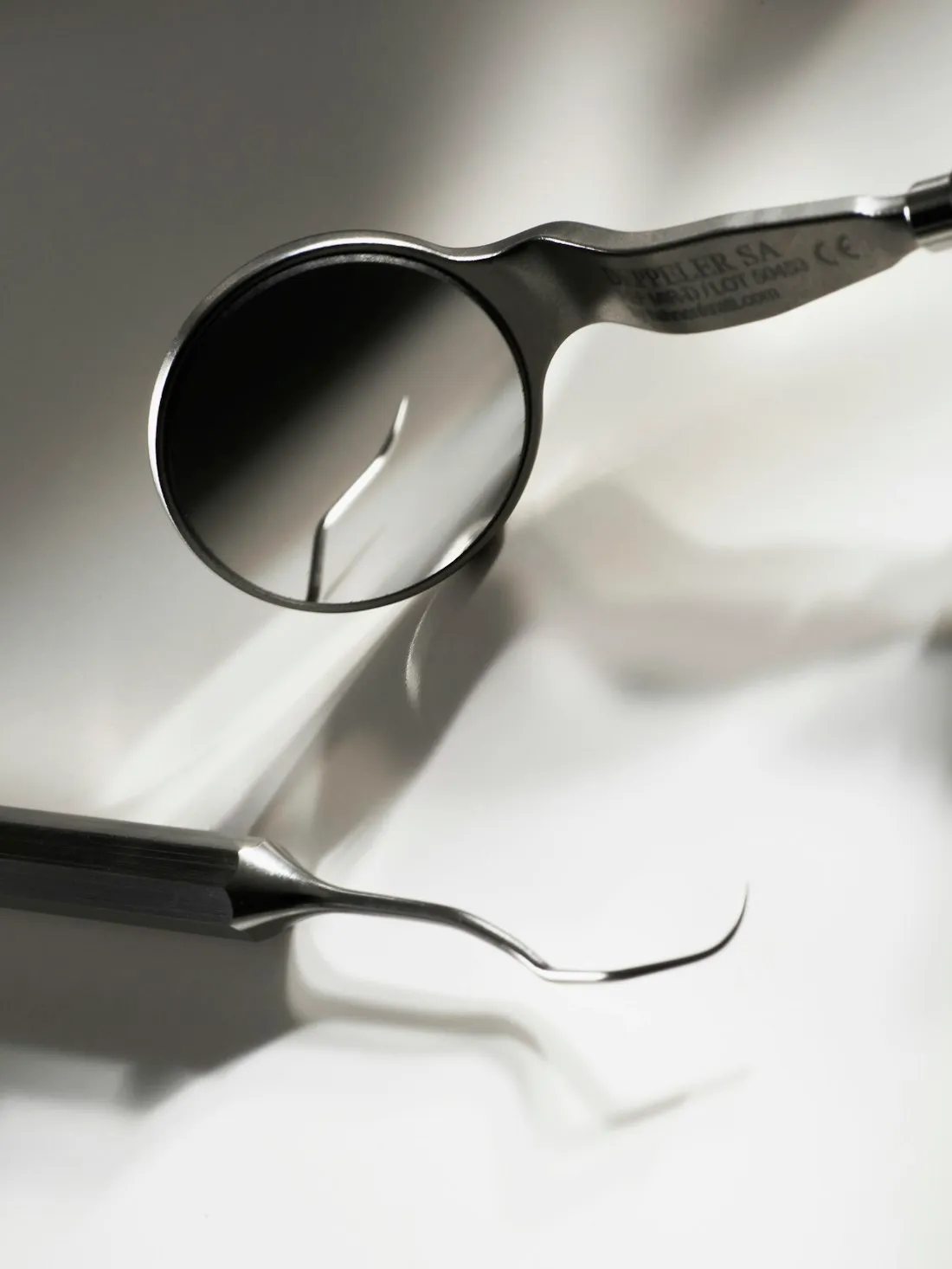 Dental mirror and periodontal probe photographed on a white surface under directional light