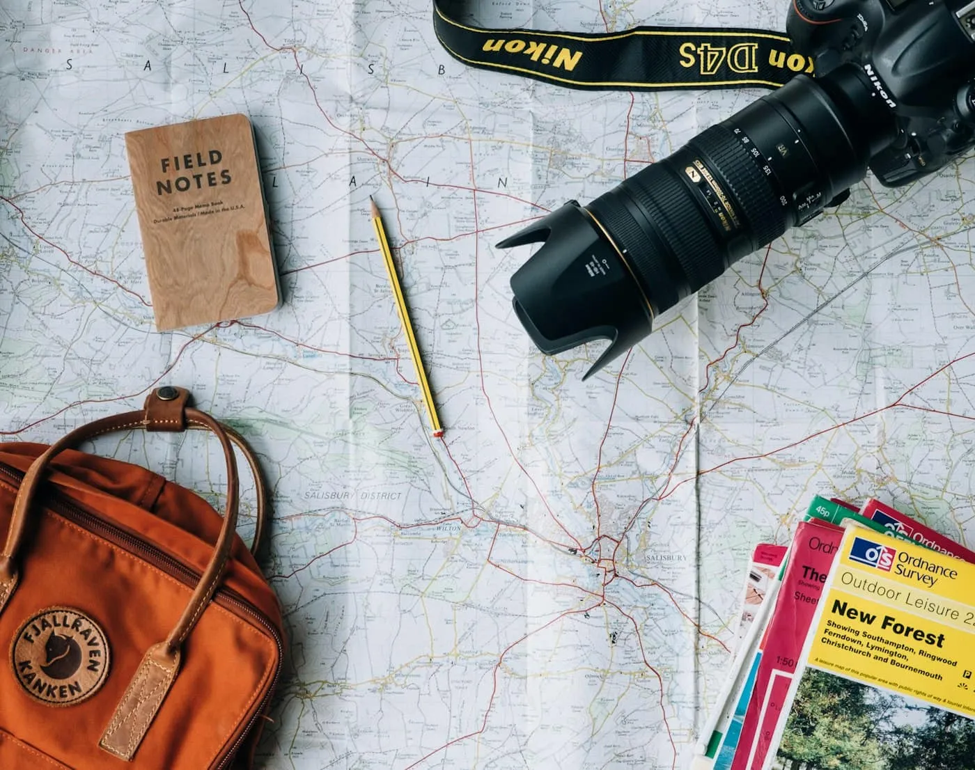 Travel flat lay with a paper map, camera, backpack, field notebook and guidebooks