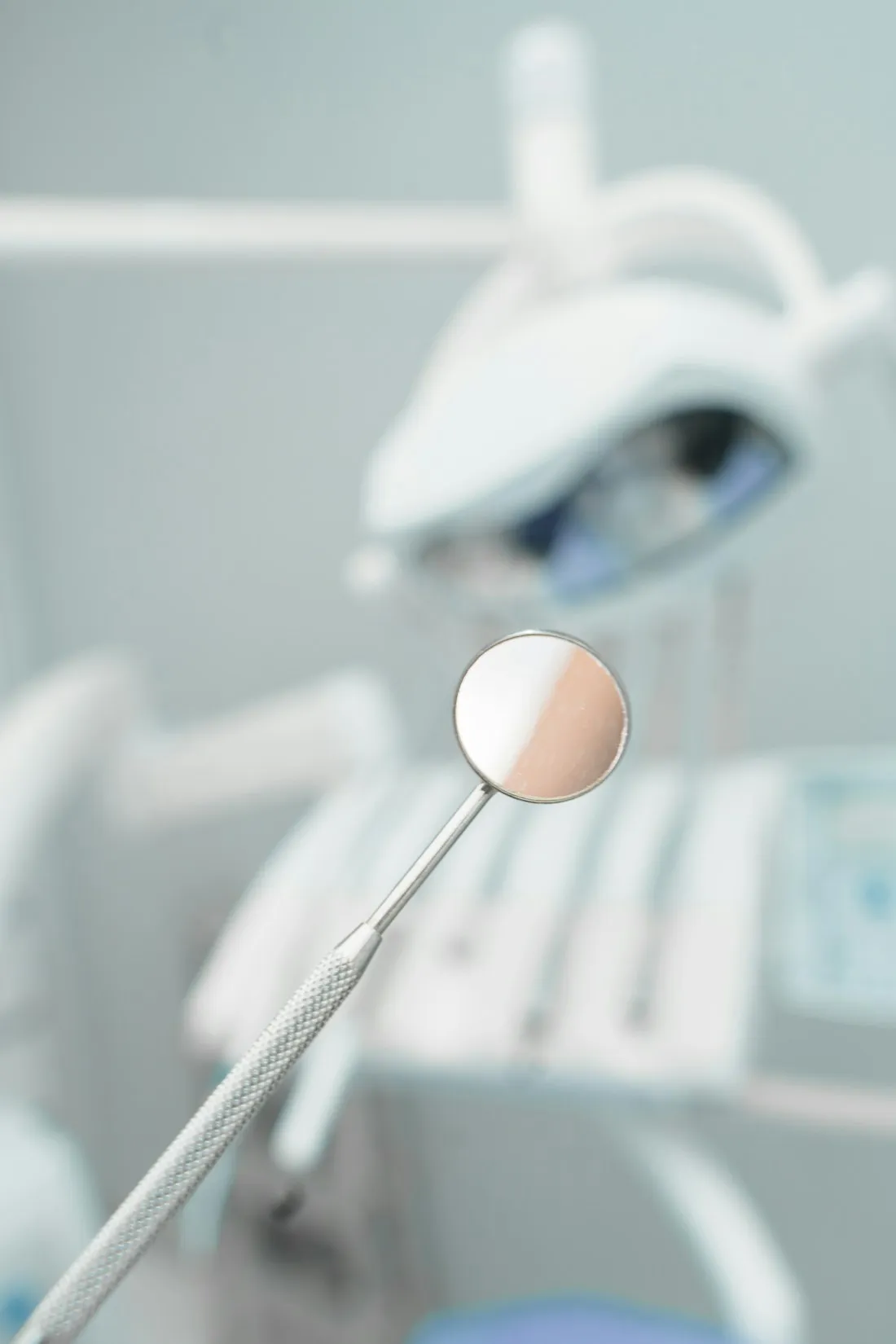 Dental mirror held in sharp focus with a treatment light softly blurred behind it
