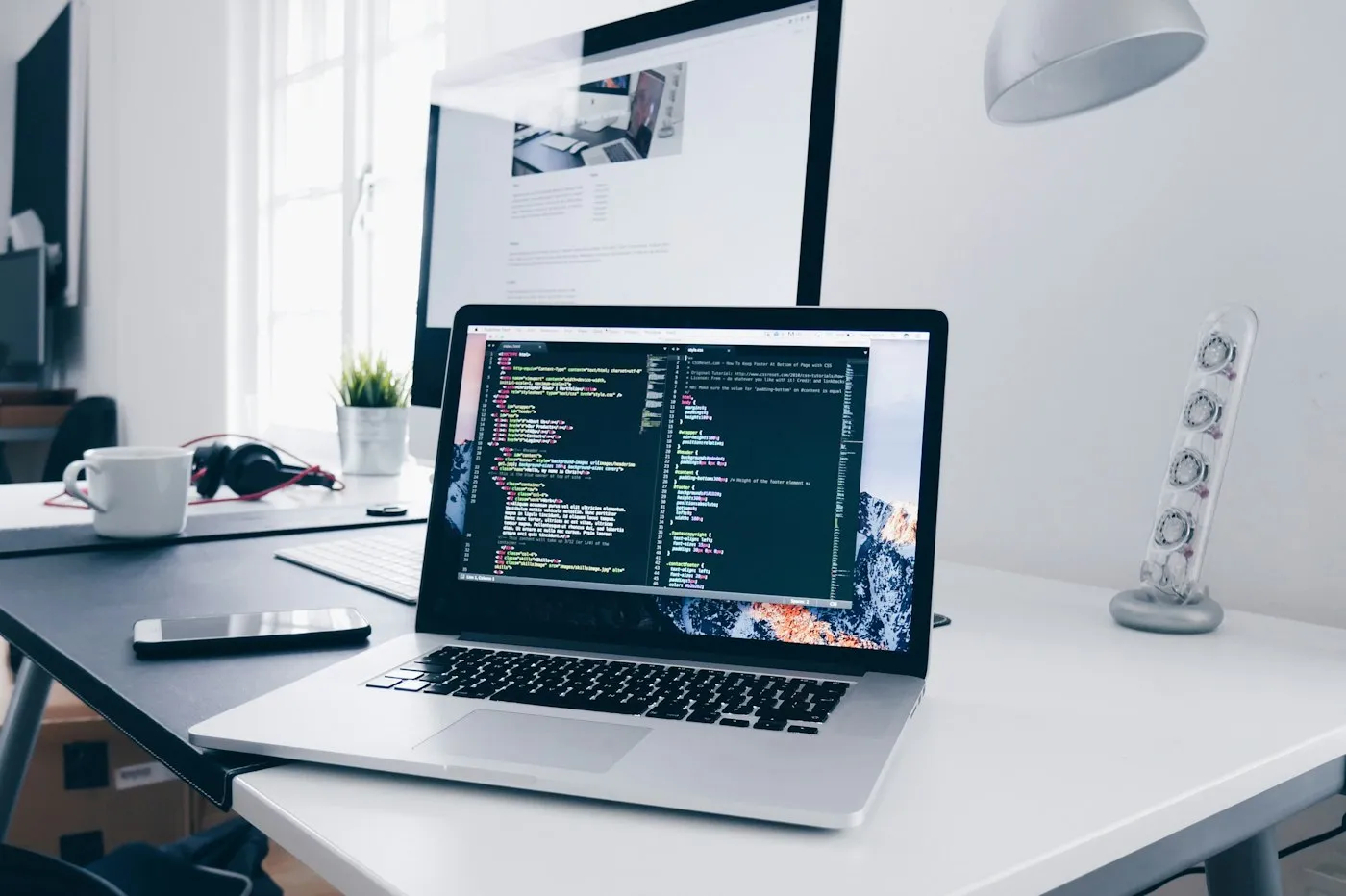 Laptop showing code on a tidy white desk beside a coffee cup