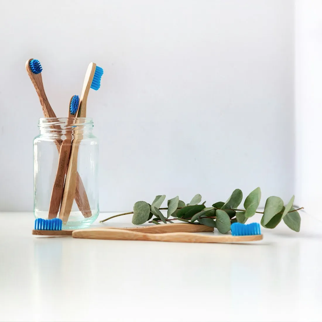 Bamboo toothbrushes standing in a glass jar beside a eucalyptus sprig